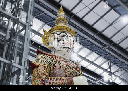 Un colorato statua raffigurante un orco gigante custode in piedi in contrasto l'argento architettura industriale in aeroporto suvannbhumi bangkok, Thailandia Foto Stock