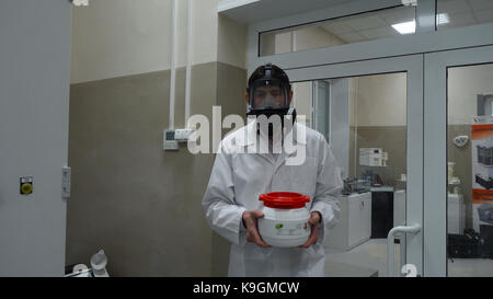 Scienziato indossare tuta protettiva e portante un barattolo di liquido tossico all'interno di un area di rischio biologico Foto Stock