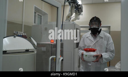 Scienziato indossare tuta protettiva e portante un barattolo di liquido tossico all'interno di un area di rischio biologico Foto Stock