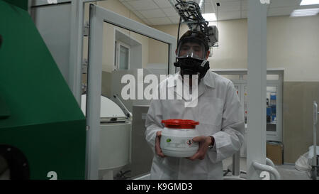 Scienziato indossare tuta protettiva e portante un barattolo di liquido tossico all'interno di un area di rischio biologico Foto Stock