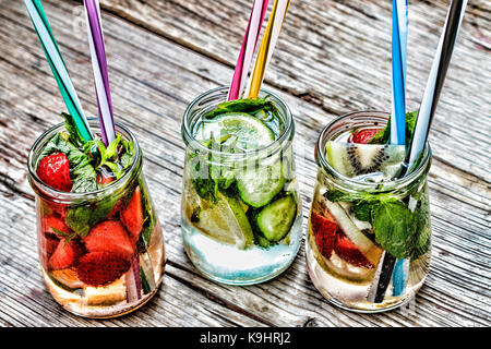 Una varietà di bevande fredde in piccoli flaconi con pezzi di frutta sullo sfondo di legno Foto Stock