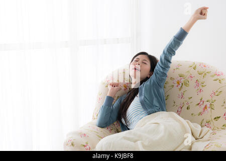 Giovane donna graziosa in appoggio il risveglio stretching corpo quando lei seduta sul divano davanti alla finestra rilassante durante le vacanze. Foto Stock