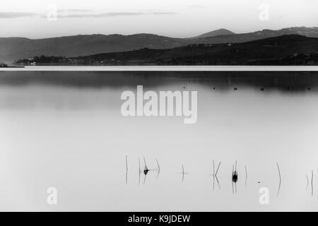 Un lago al tramonto con luce morbida, lontane colline e montagne, reti da pesca in primo piano e un sacco di spazio vuoto Foto Stock