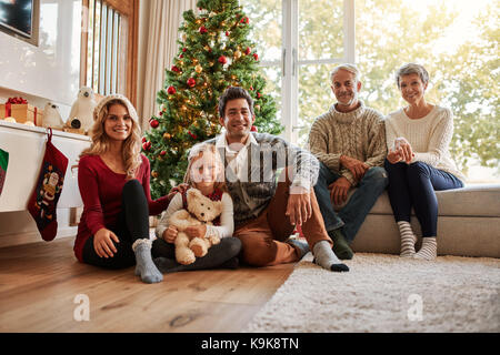 Ritratto di multi generazione famiglia nella parte anteriore dell'albero di natale. La famiglia felice seduti a casa durante il periodo di Natale. Foto Stock