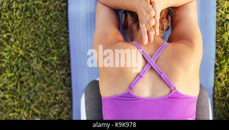 Vista superiore del fitness donna seduta sul tappetino di esercizio con le mani giunte e la piegatura in avanti. Sani di sesso femminile a praticare lo yoga all'esterno. Foto Stock