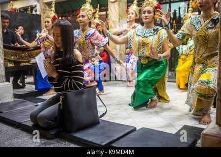 Donne che pregano, e ballerine tradizionali thailandesi che si esibiscono per Brahma, ballano su richiesta per donazioni, Erawan Shrine, Bangkok Foto Stock