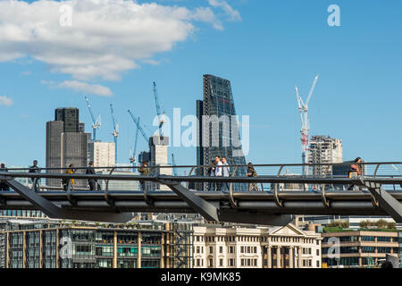 La gente camminare attraverso la passerella del millennio attraverso il fiume Tamigi a Londra Regno Unito con lo skyline della città di Londons' miglio quadrato Foto Stock