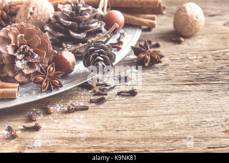 Natale decorazione vintage con bastoncini di cannella e anice stellato, coni, dadi e ornamenti natale su vintage rustico sfondo di legno, selettivo Foto Stock