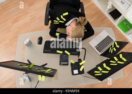 Stanco giovane imprenditrice con note di promemoria di dormire sulla scrivania in ufficio Foto Stock