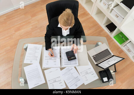 Angolo di alta vista del giovane imprenditrice calcolare le fatture in office Foto Stock