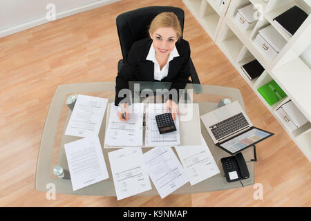 Angolo di alta vista del giovane imprenditrice calcolare le fatture in office Foto Stock