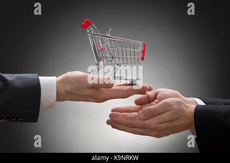 Close-up di imprenditore dando a mano mini carrello ad altri commercianti Foto Stock