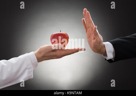 Close-up di mano di una persona che rifiuta di rosso Apple terrà dal medico Foto Stock