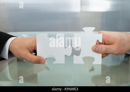 Close-up di due proprietari mani puzzle sulla scrivania in ufficio Foto Stock