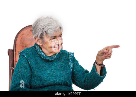 Vecchia donna poiting il suo nottolino sinistro a qualcosa e cercando di esso, isolata contro uno sfondo bianco. Foto Stock