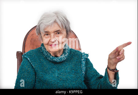 Vecchia donna poiting il suo nottolino sinistro a qualcosa e guardando la telecamera, isolata contro uno sfondo bianco. Foto Stock