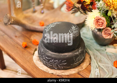 Confezione, decorazione, vacanze concetto. sulla celebrazione tabella vi è incantevole torta di nozze di straordinario colore nero con dipinto di bianco di elementi di forma di foglie sulle attrazioni turistiche Foto Stock