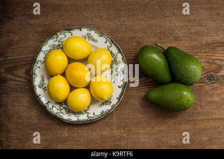 Vista superiore colpo di limoni posti in piastra bianca con verde ornamento e tre gli avocadi oltre rustico sfondo di legno Foto Stock