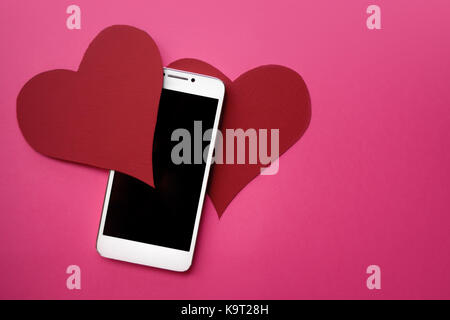 Cuori e smartphone. Il concetto di simili in reti sociali o dating app. sfondo rosa Foto Stock