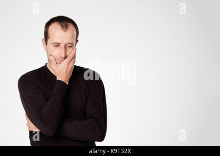 Uomo caucasico in camicia nera guardando in giù con emozione scettico sul viso. Foto Stock