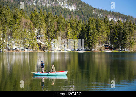 Due pescatori in barca a remi sul lago spitzingsee di fronte montagne innevate e foreste di montagna in primavera, Baviera, Germania Foto Stock