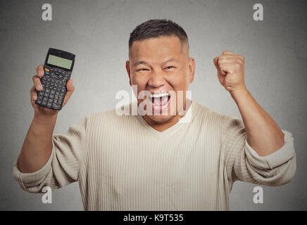 Emozionato happy business uomo persona che mostra la calcolatrice con milioni di segno di numero sullo schermo isolato sul muro grigio office background. Volto umano espressione Foto Stock