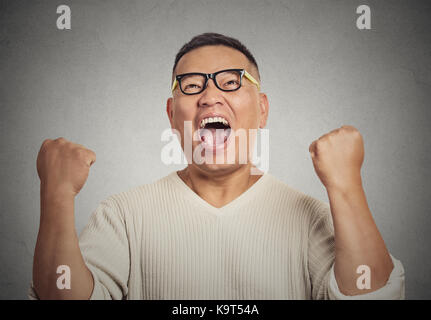 Closeup ritratto studente di successo con gli occhiali uomo vincente, pugni pompato per celebrare il successo isolato muro grigio Sfondo. positiva emozione umana f Foto Stock