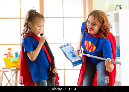 Donna felice e sua figlia si sta preparando per la pulizia della camera. La madre e il figlio di lei ragazza che gioca insieme. famiglia in costumi di supereroi. Foto Stock