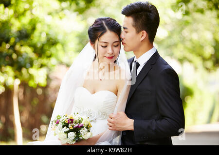 Giovani asiatici groom kissing sposa all'aperto durante la cerimonia nuziale. Foto Stock