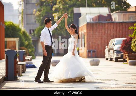 Giovani asiatici sposa e lo sposo in abito da sposa in ballo nel parcheggio. Foto Stock