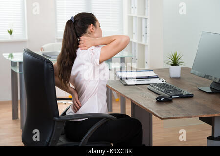 Giovane imprenditrice seduti su una sedia avente backpain in office Foto Stock