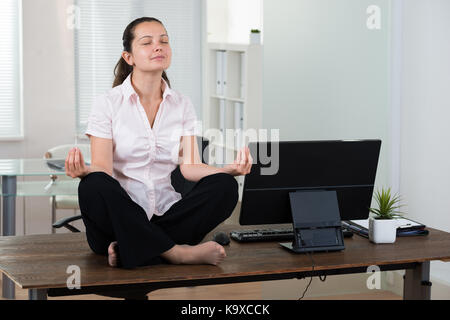 Giovane imprenditrice facendo la meditazione sulla scrivania in ufficio Foto Stock