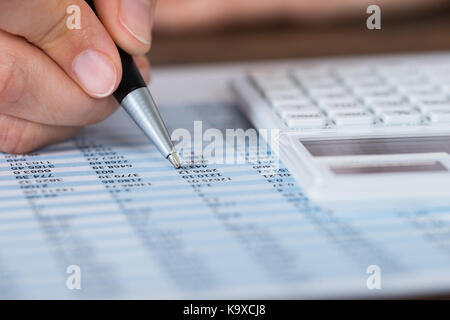 Close-up di persona mani tenendo la penna con la calcolatrice sulla relazione finanziaria Foto Stock