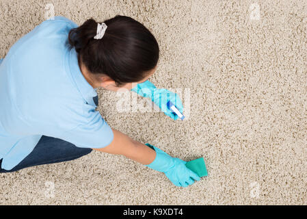 Giovane donna Pulizia tappeto con detergente spray Flacone e spugna Foto Stock