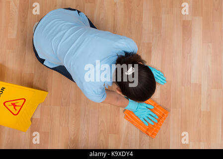 Elevato angolo di visione della donna di sfregamento del pavimento in legno con un panno Foto Stock