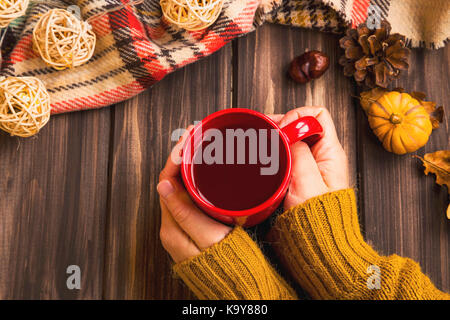 Impostazione di caduta donna mani tenendo calda tazza di tè con vintage coperta caduta su sfondo di legno e zucca deco,accogliente autunno flatlay impostazione Foto Stock