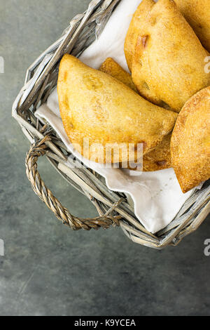 In casa pane appena sfornato empanadas fatturato torte con pisto vegetali ripieno di formaggio in salsa di pomodoro in cesto in vimini. Spagnolo. pasta di cemento scuro sto Foto Stock