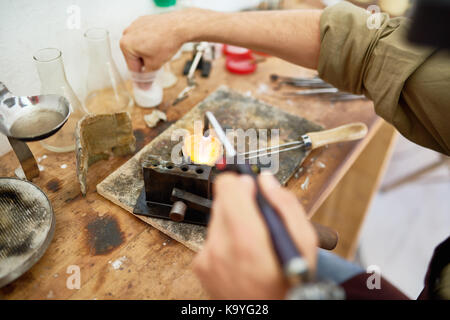 Primo piano delle mani maschio metallo in fusione nel bicchiere mentre i gioielli di colata a workstation Foto Stock