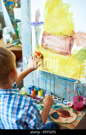 Vista posteriore ritratto di Little Boy fingerpainting casa usando acquerelli su cavalletto in art studio Foto Stock