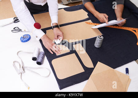 Elevato angolo di visione di un irriconoscibile designer rendendo pattern sul tessuto con tailors chalk mentre rendendo camicia maschile, il suo collega in piedi accanto a lui un Foto Stock