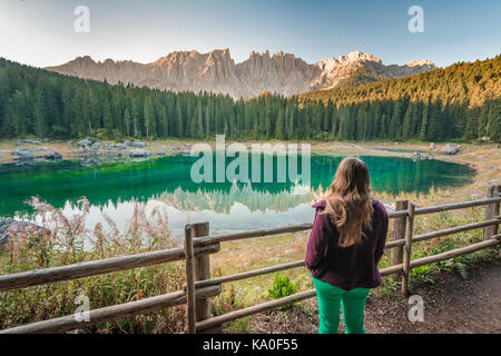 Donna si affaccia sul Lago Carezza, Lago di Carezza, sole mattutino, Gruppo Latemar riflesso nel lago, cime della montagna Torre Diamantidi Foto Stock