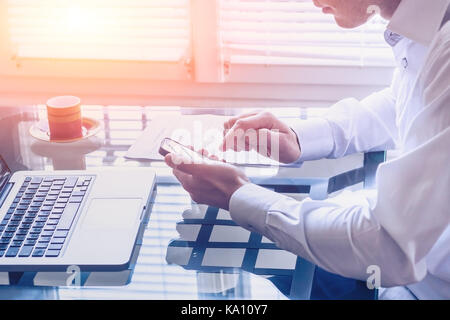 Imprenditore lavora in un ufficio moderno con lo smartphone e il computer portatile di mettersi in contatto con il suo team aziendale Foto Stock