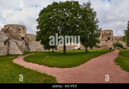 Un antico muro di fortificazione con torri di avvistamento. prima che il muro cresce un albero a foglie decidue con una corona circolare. russia, Pskov Regione Foto Stock