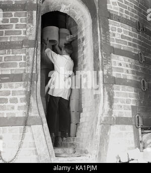 1950, storico lavoratore mettendo in ceramica per essere sparato all'interno di un grande forno di mattoni a Belleek Pottery Company, County Fermanagh, Irlanda del Nord. L'attività iniziata nel 1857, è uno del paese stabilito più lunga e famosa azienda. Foto Stock