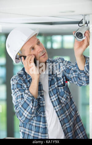 Maschio maturo tecnico che installa la fotocamera del telefono Foto Stock