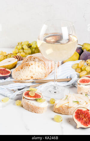 Panini con ripieno di ricotta o formaggio spalmabile, ciabatta, fichi freschi, pere, uva, noci e miele su marmo bianco tabella tabella, con bicchiere di vino spazio copia Foto Stock