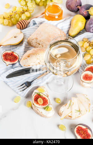 Panini con ripieno di ricotta o formaggio spalmabile, ciabatta, fichi freschi, pere, uva, noci e miele su marmo bianco tabella tabella, con bicchiere di vino spazio copia Foto Stock