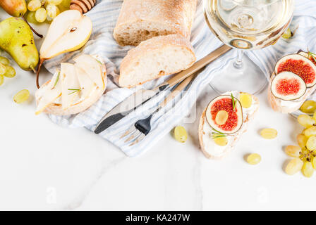 Panini con ripieno di ricotta o formaggio spalmabile, ciabatta, fichi freschi, pere, uva, noci e miele su marmo bianco tabella tabella, con bicchiere di vino spazio copia Foto Stock