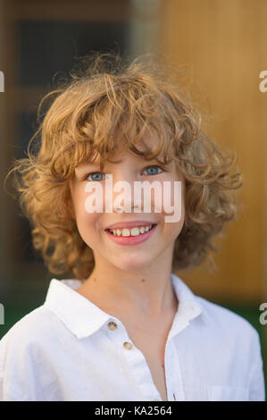 Ritratto del bel ragazzo di 10-11 anni. Il compagno ha bellissime fair capelli ricci, blu occhi allegri, abbronzato pelle, un sorriso piacevole. Il ragazzo è il dott. Foto Stock