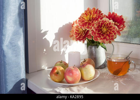 Autunno still life con red dalie in un barattolo di latta, zucca, una tazza di tè e mele sulla finestra in tempo soleggiato Foto Stock